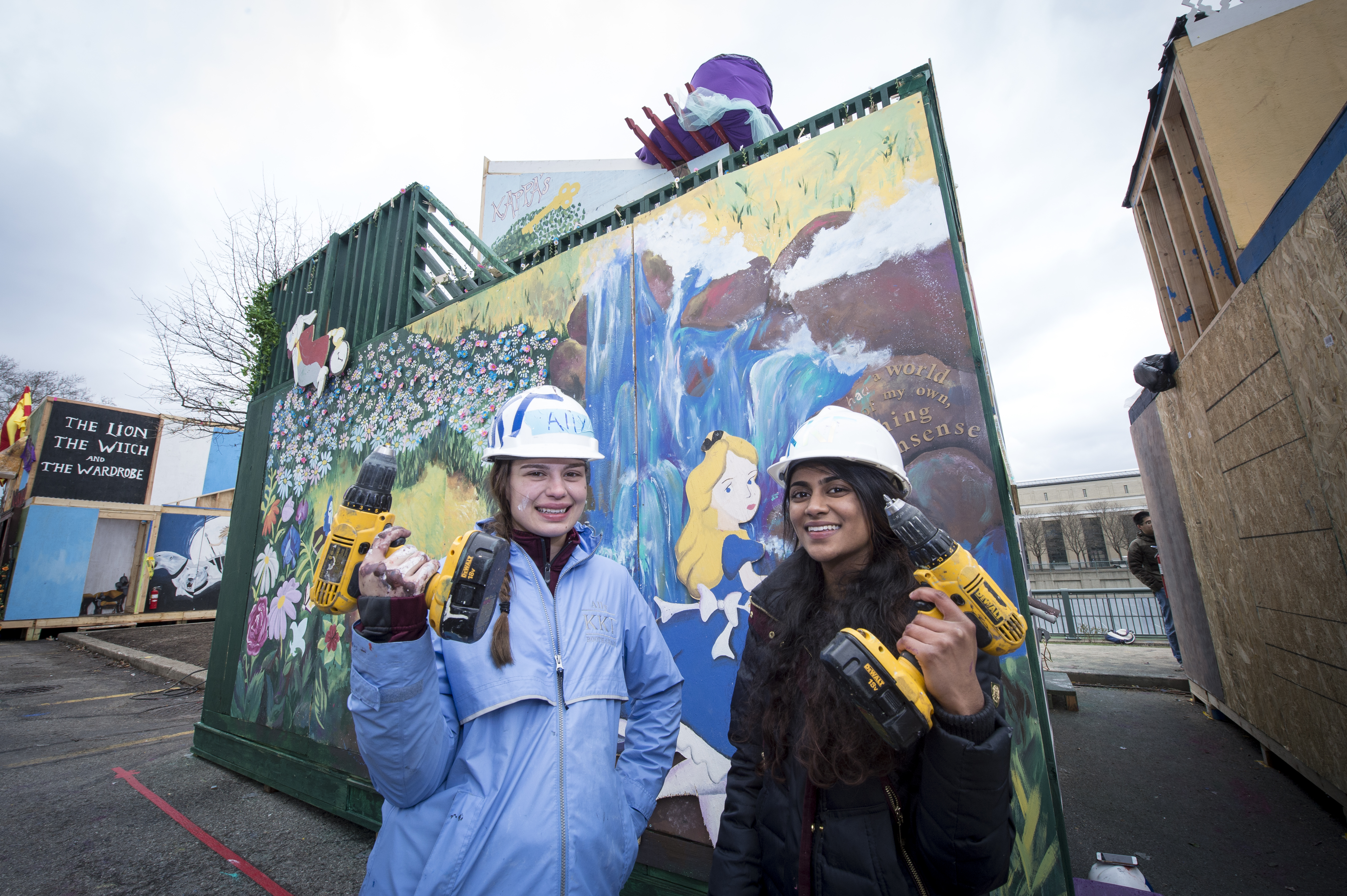 Photo of two female students with drills, posing in front of the booth they are building