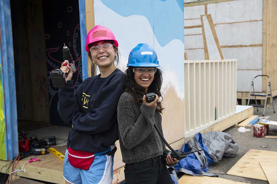 Photo of two female students, posing in front of the booth they are building