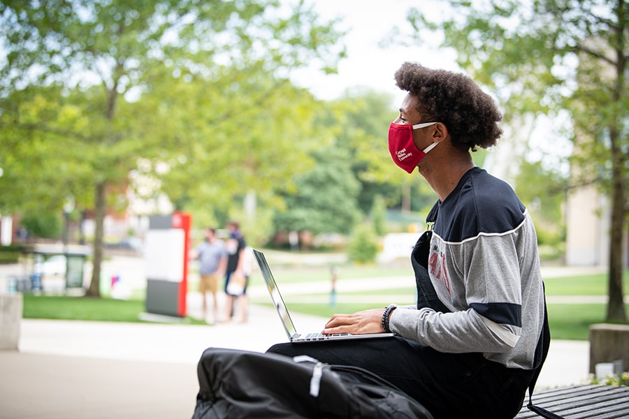 a CMU student with a face covering on working on a laptop on campus on a sunny day