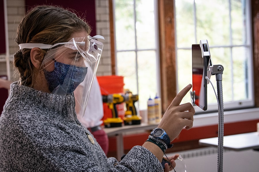 a student wearing a face shield looking at an iPad
