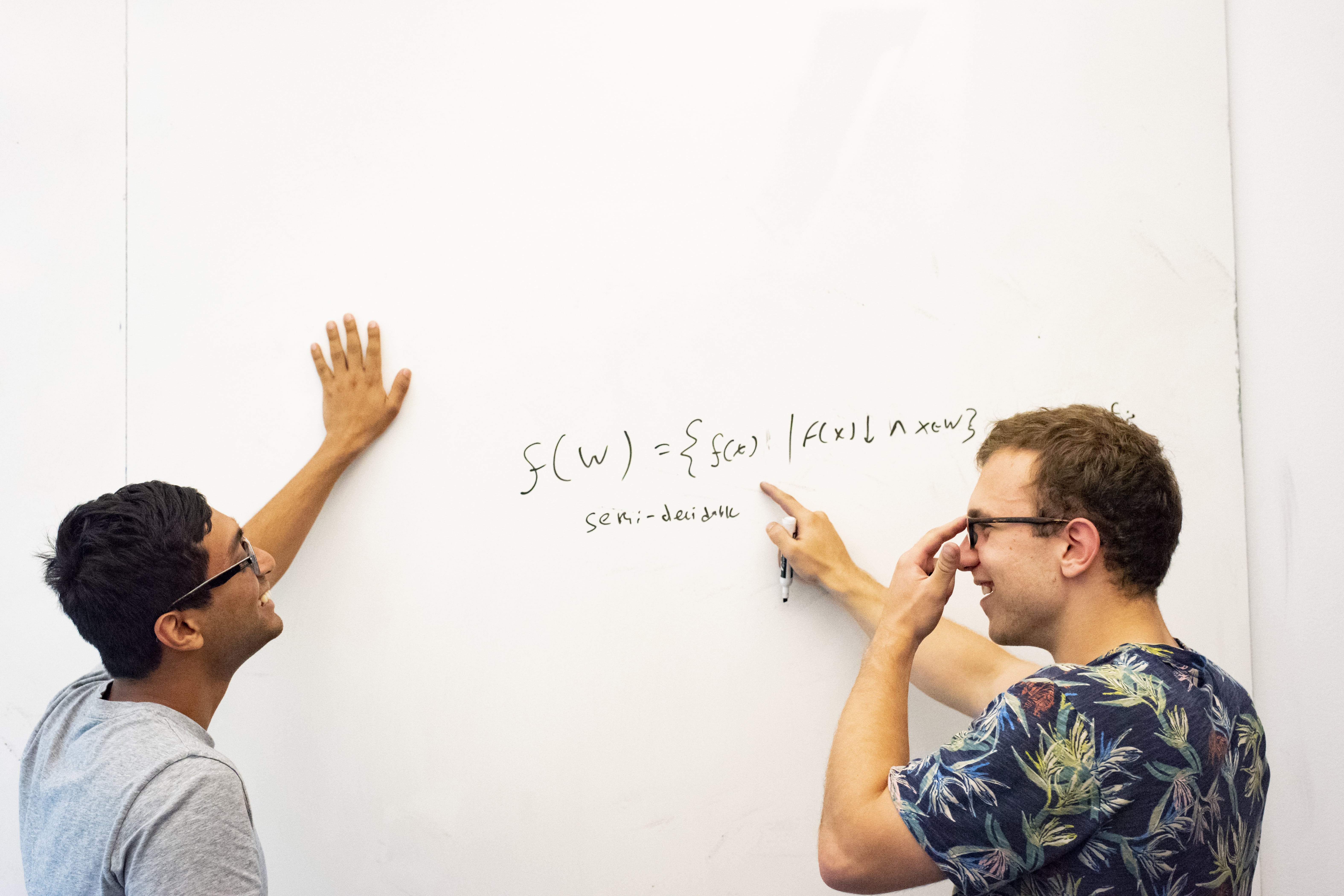 two students working on a white board with a safe distance between them