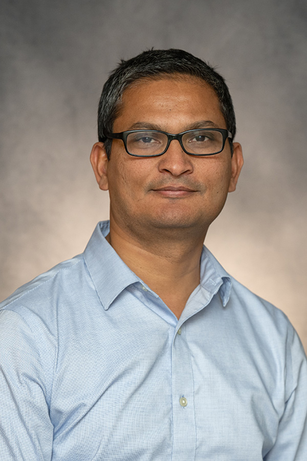 Simranjeet Singh smiles for the camera. He is wearing glasses and a blue button-down shirt.