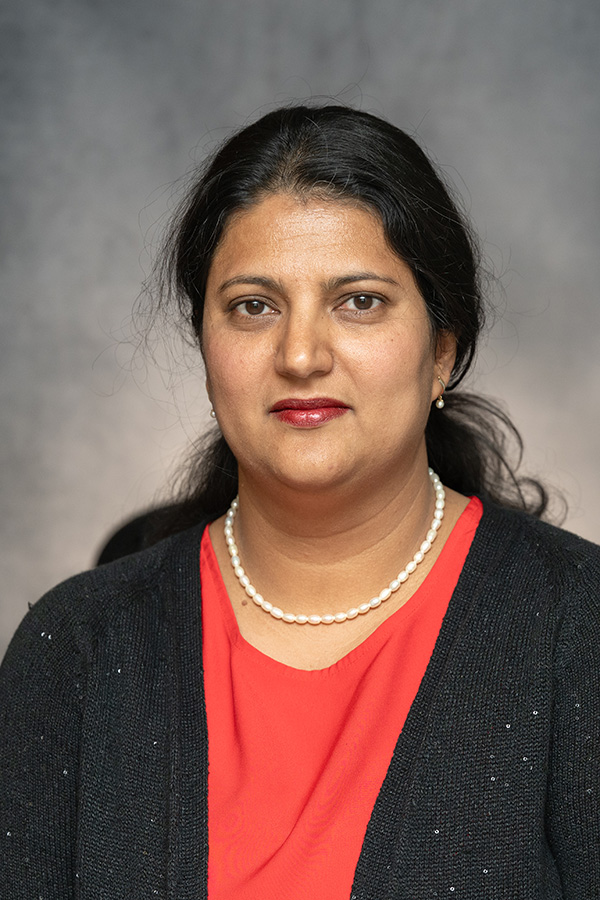 Jyoti Katoch looks at the camera. She is wearing a red blouse, black blazer and a string of pearls.