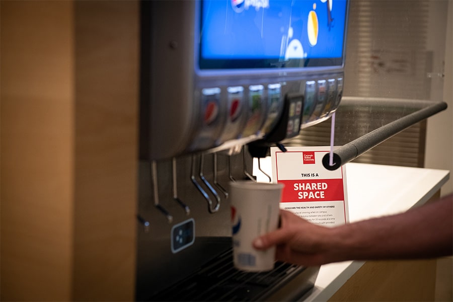 Image of hand and cup getting soda from a soda machine from behind plexiglass