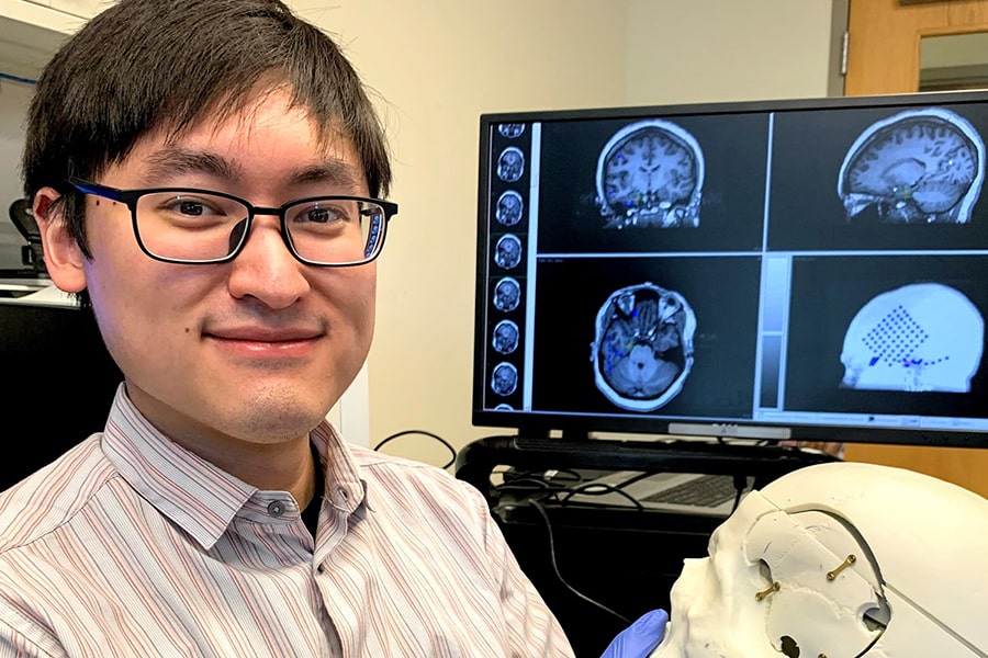 environmental portrait of Maxwell Wang holding a model of a skull with brain images on a computer screen in the background