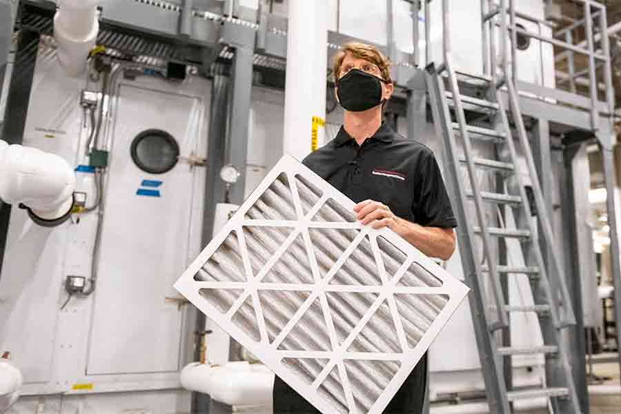 Image of University Engineer Steve Guenther masked and holding an air filter inside Tepper's boiler room