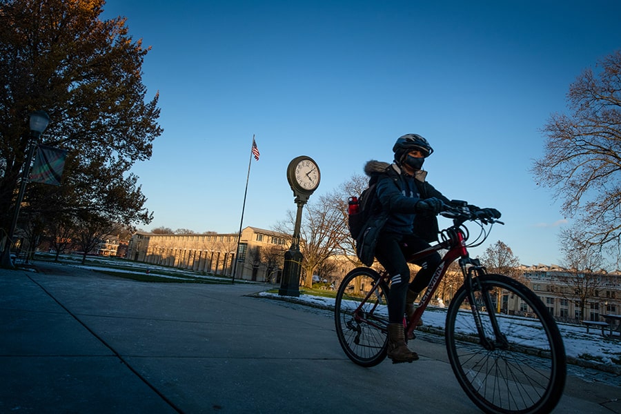 person riding bike past the clock on campus at dusk