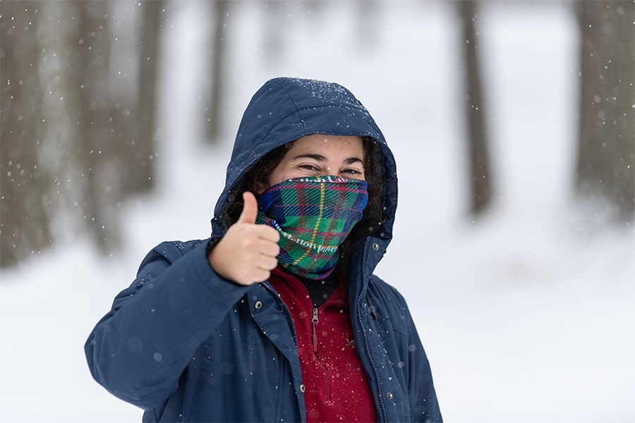 student wearing Tartan mask outdoors in snow giving thumbs up sign 