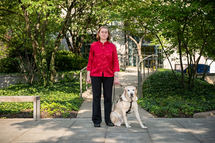 image of Catherine Getchell standing with guide dog in front of greenery on campus
