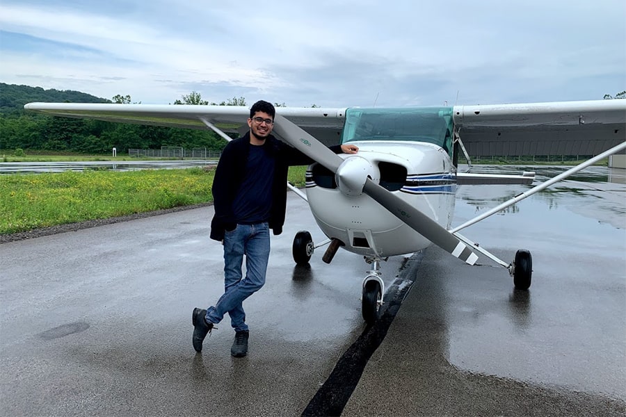 Jay Patrikar leaning on a small plane on the tarmac on an overcast day