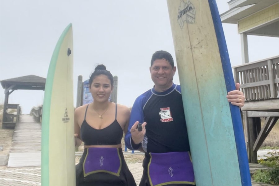 Eliana and Gary holding their surfboards