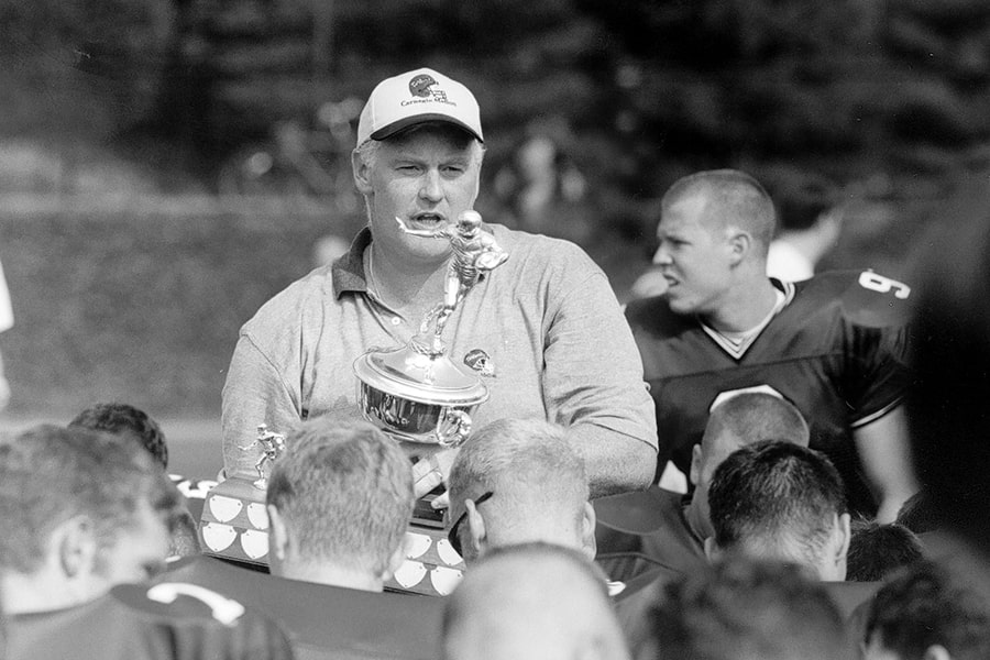 Rich Lackner holds a trophy and talks to the team