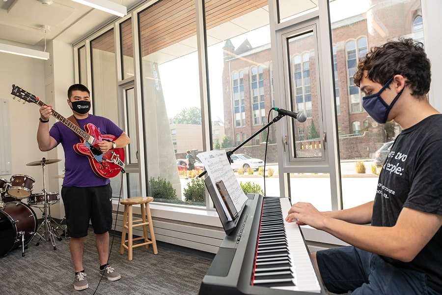 two students playing piano and guitar in common area 