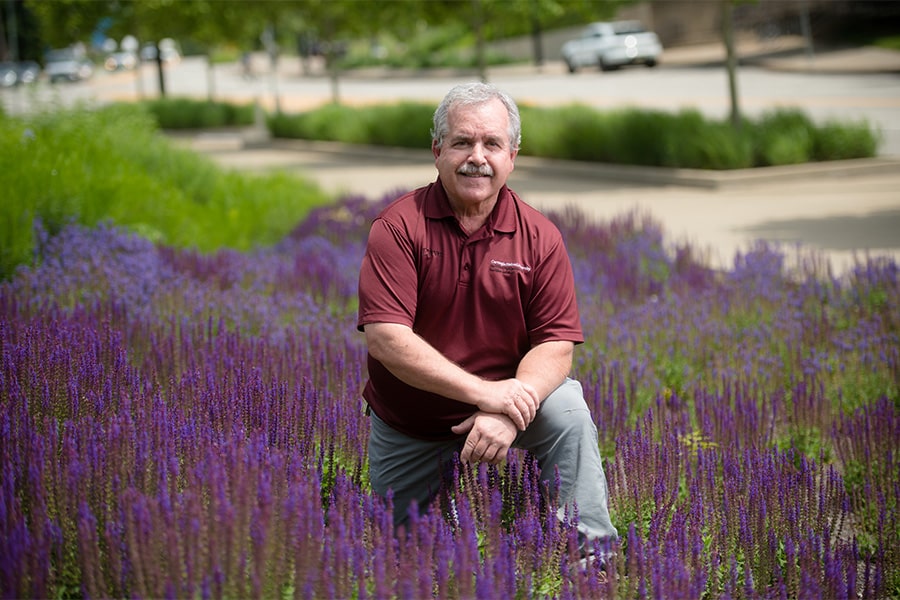 David Wessell kneeling in a flowerbed on the Tepper Quad