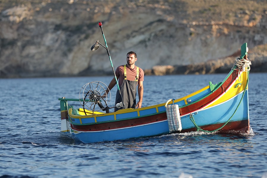 a fisherman stands in his wooden fishing boat in "Luzzu." 