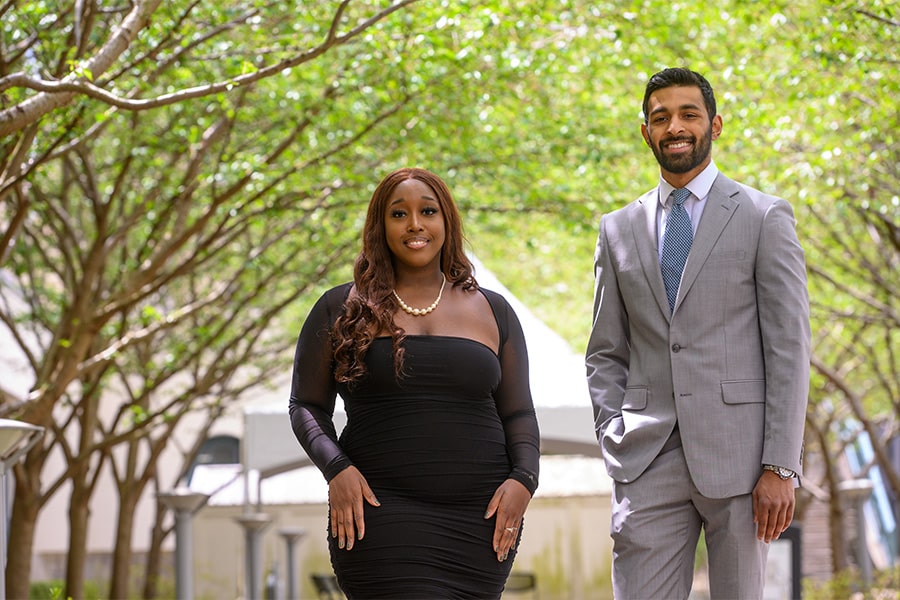 student speakers standing wearing business casual dress with spring trees in background