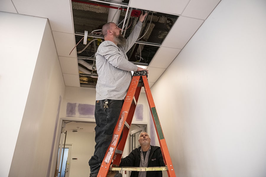 Facilities staff on ladder repairing a pipe