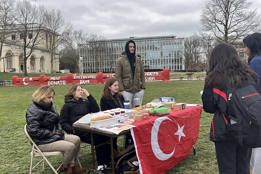 students behind a table of baked good on the Cut with the Fence in the background