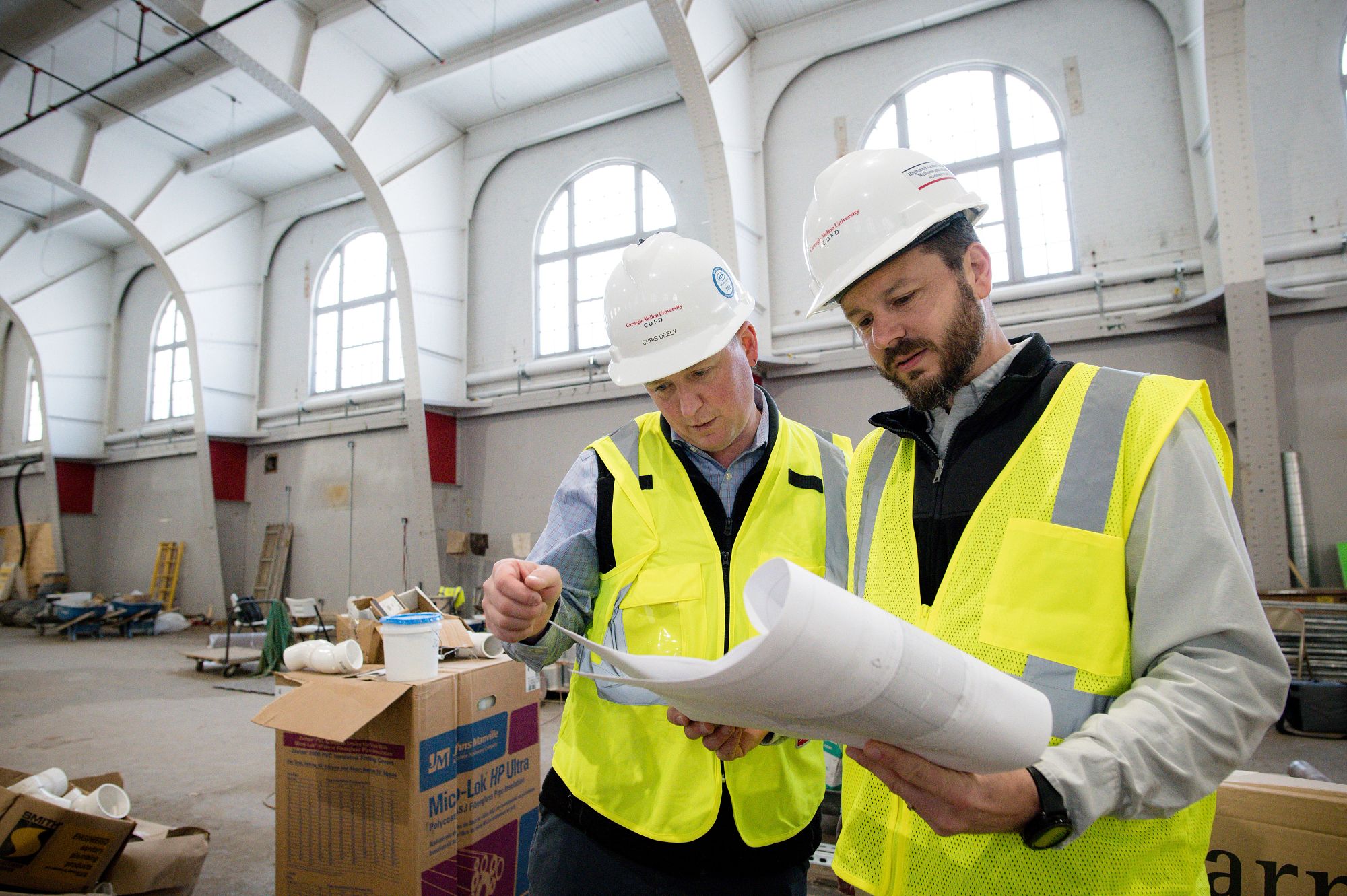 Two workers working together and looking at layouts at a construction site for a CMU building.