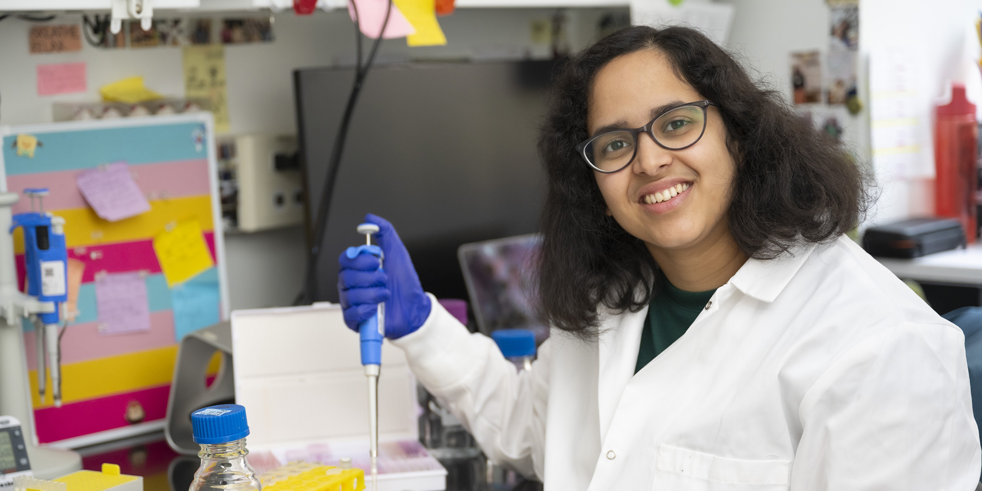 Samskrathi Sharma works in the lab and smiles at the camera.