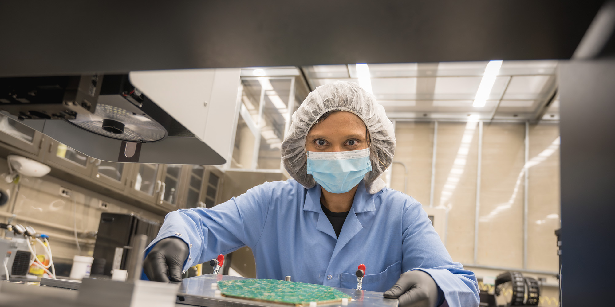 An image of a woman in a lab wearing safety gear and holding a hexagon tile.