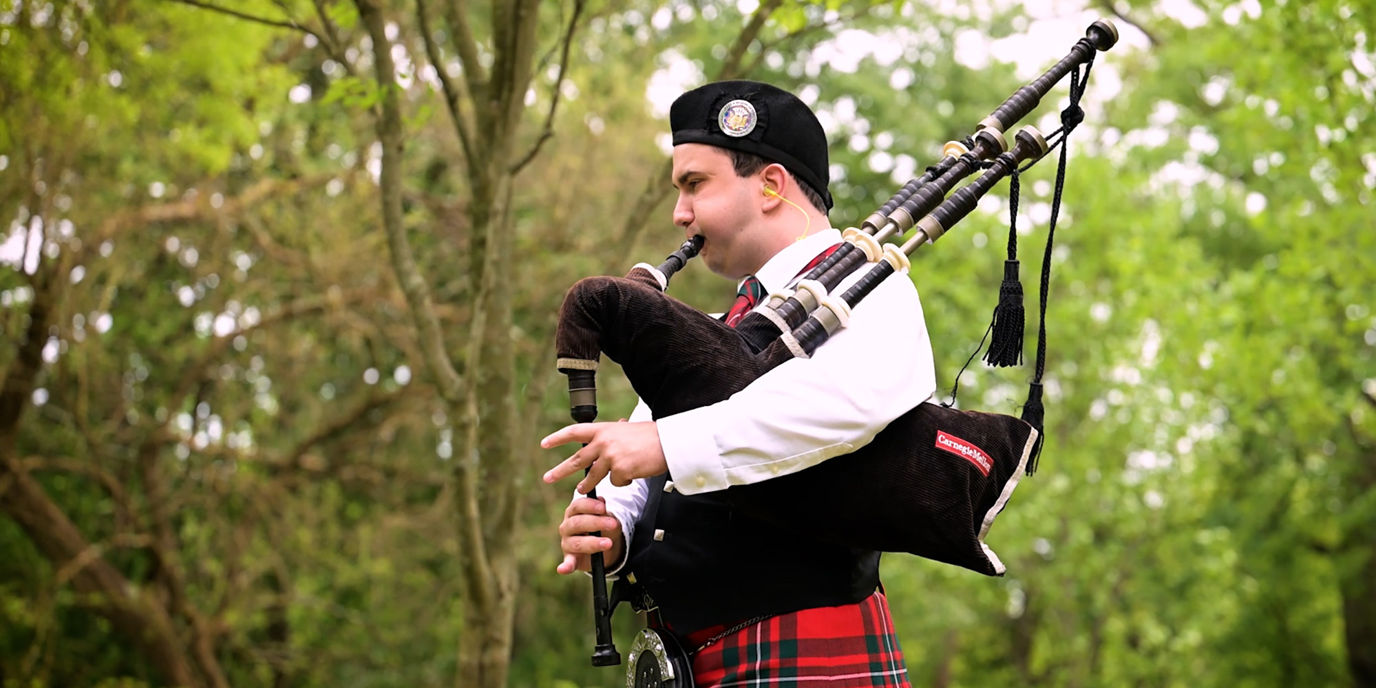 Logan McGregor stands outside and plays the bagpipes.