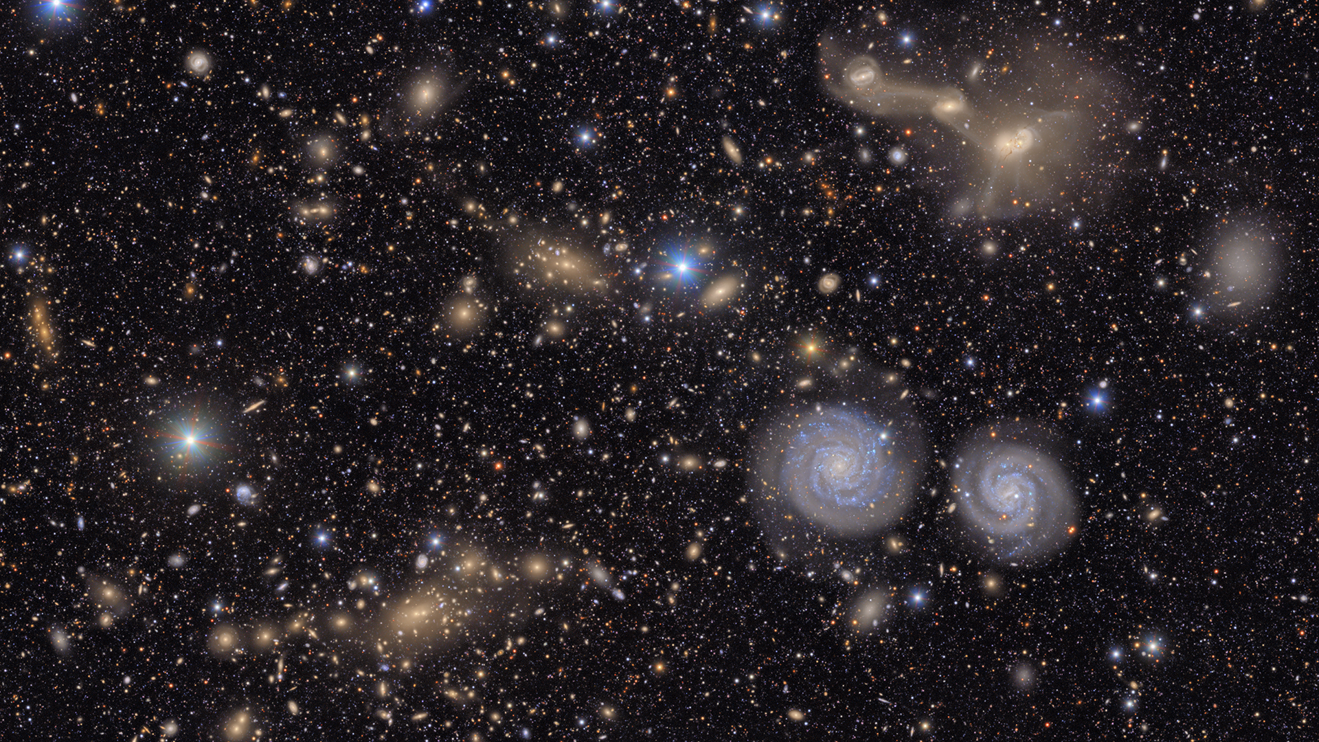 Many stars and galaxies including two spiral galaxies and three merging galaxies.