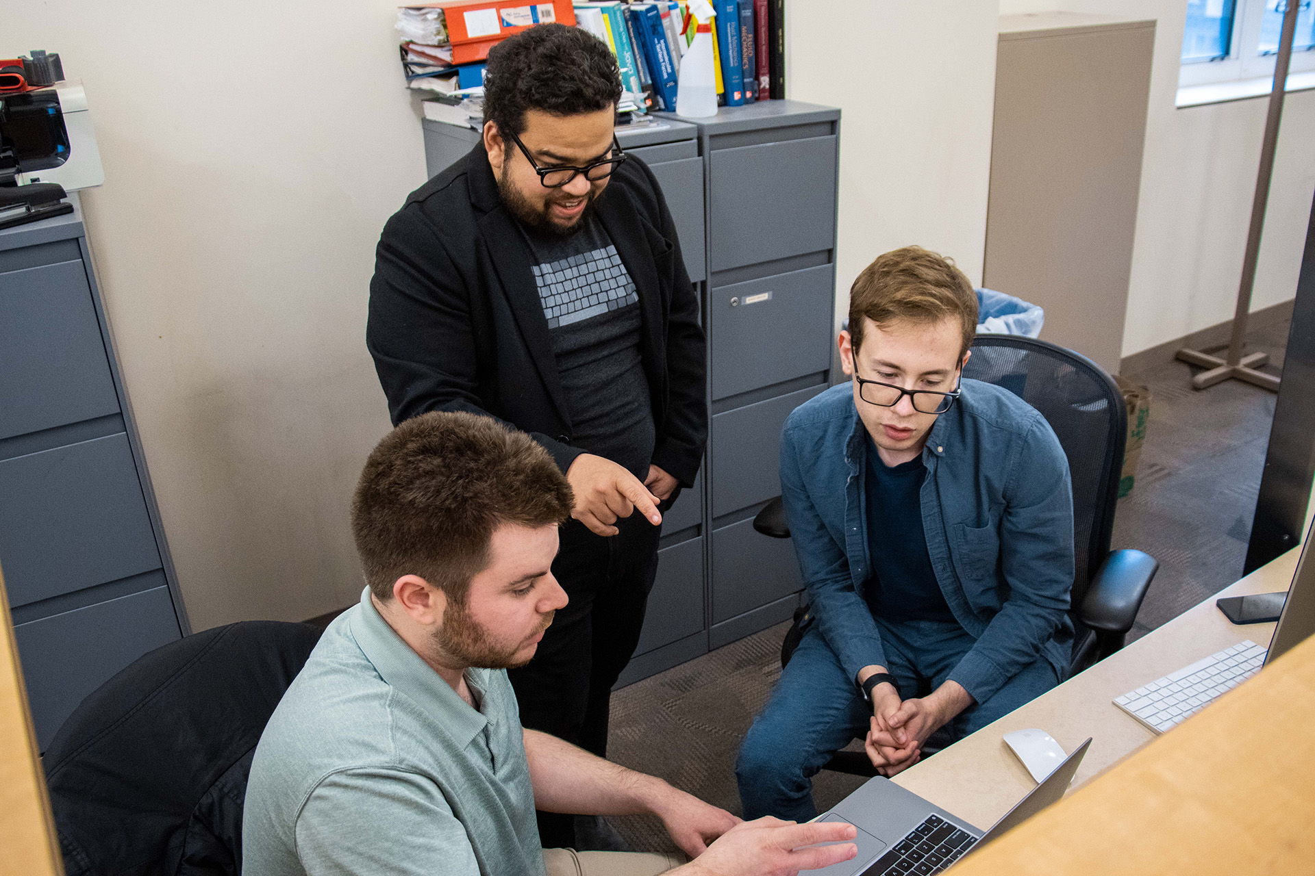 Gabe Gomes, Robert MacKnight and Daniil Boiko gather around a computer.