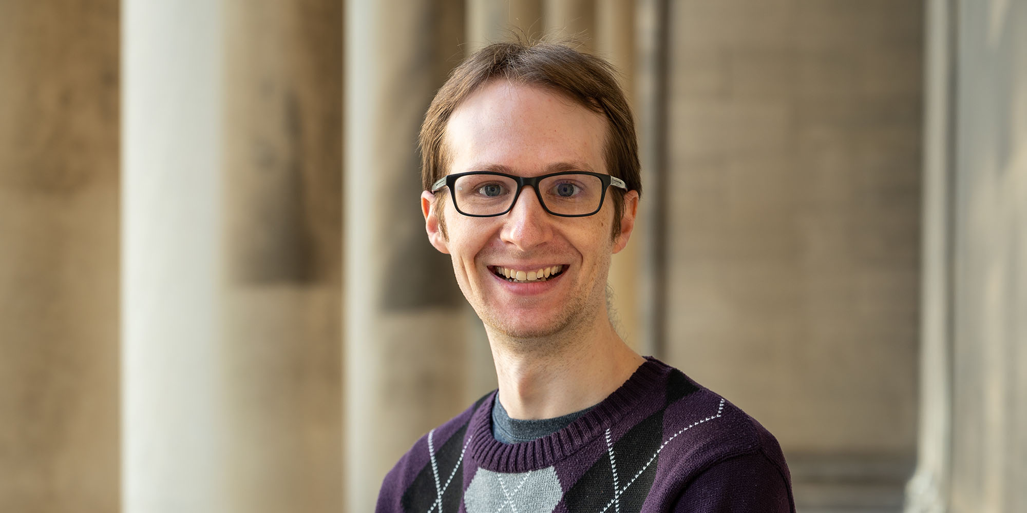 Image of a man standing by sand colored building columns.