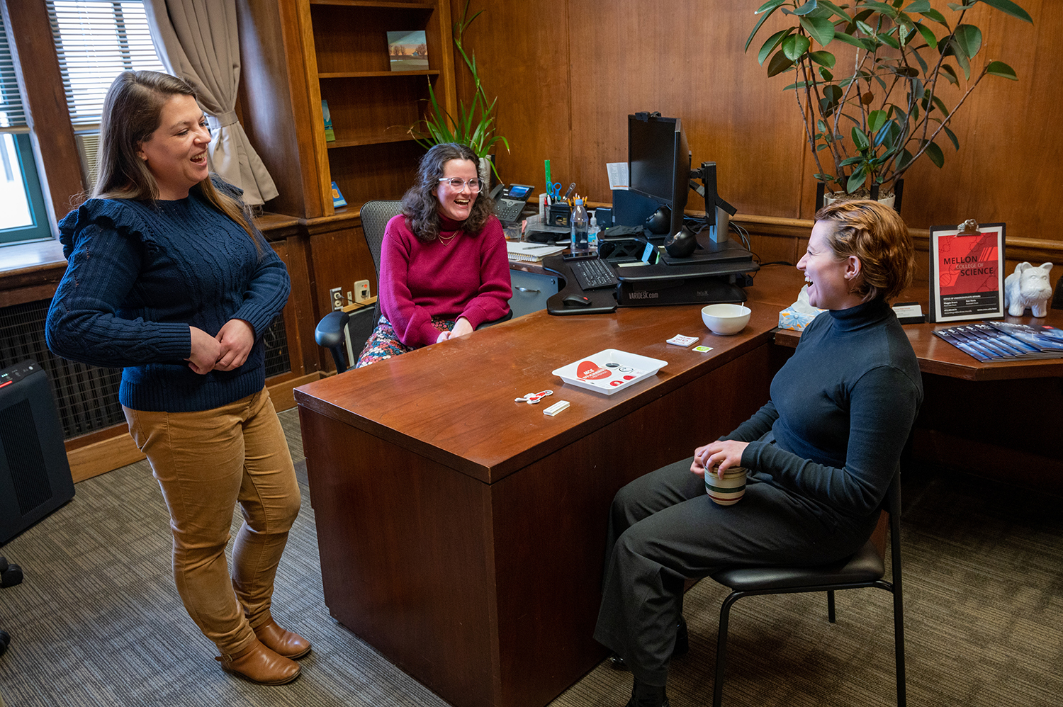 Three women engaged in lively conversation and laughter in an office setting.