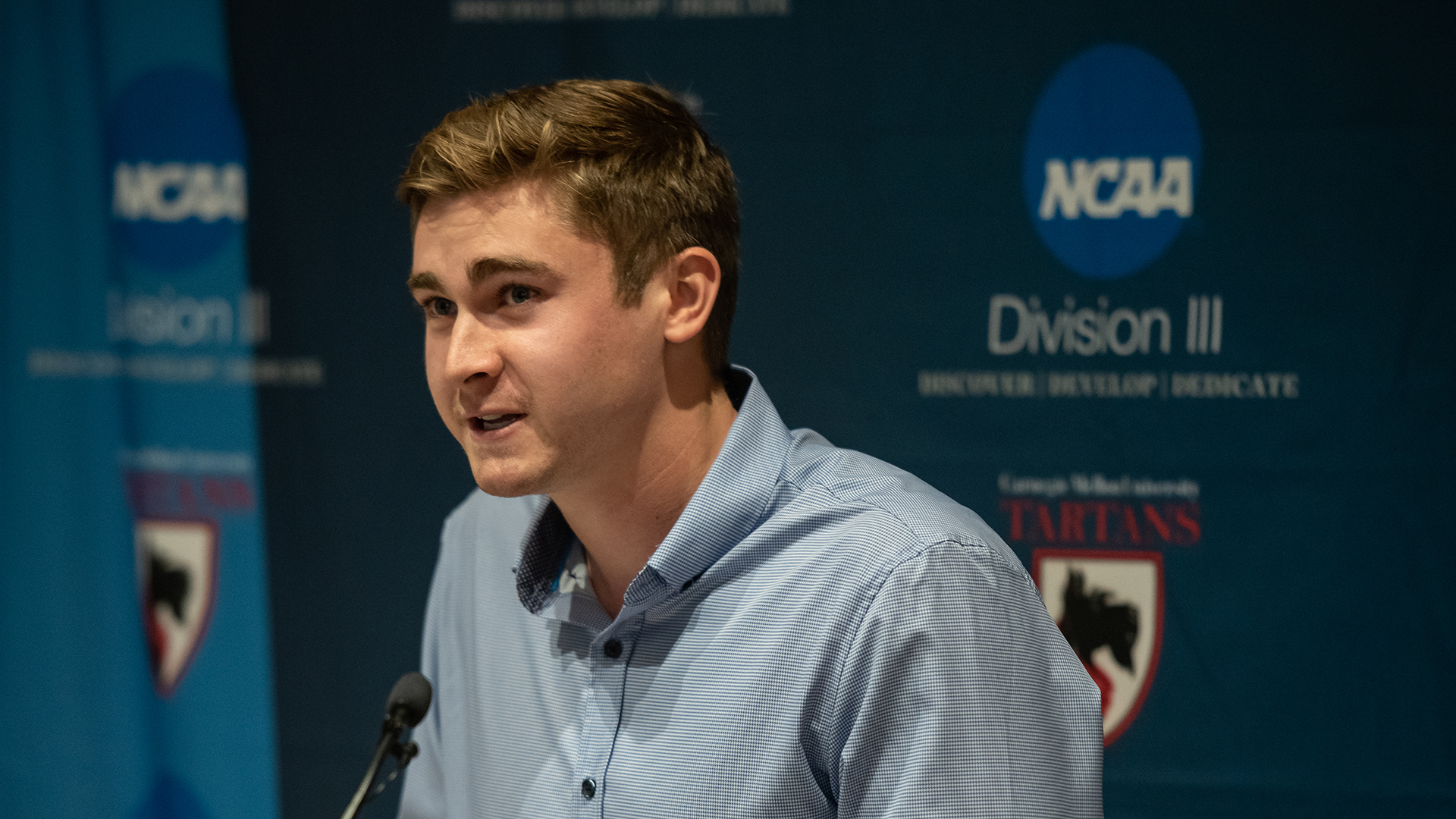 Mason Shockley sits in front of a Carnegie Mellon Tartans NCAA Division III background and speaks into a microphone.