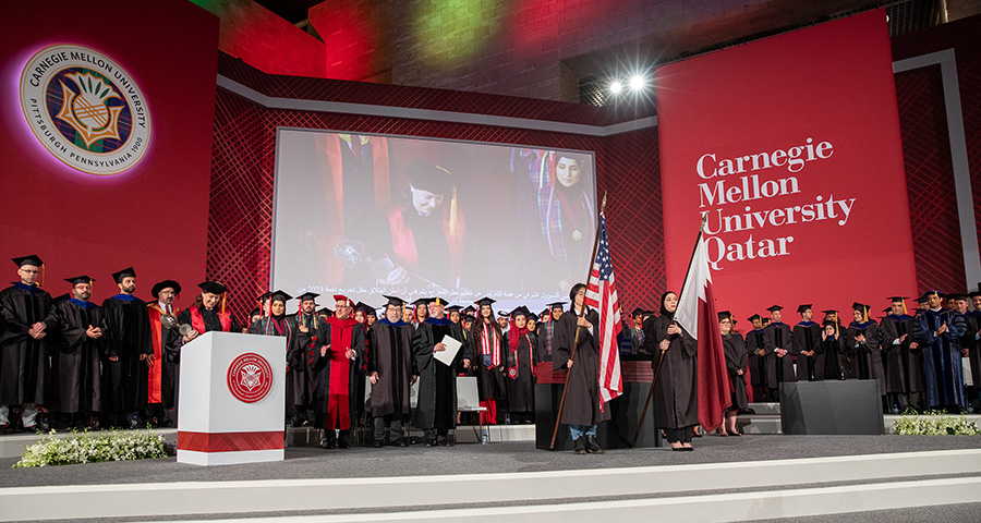 A large group of graduates stand on stage.