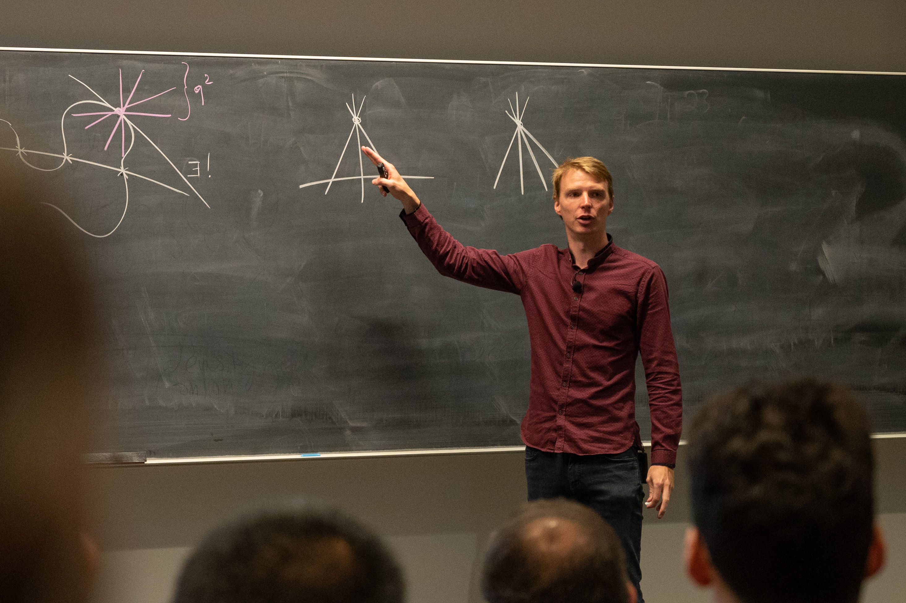 Sam Mattheus stands in front of a blackboard and explains a math concept to a room of people.