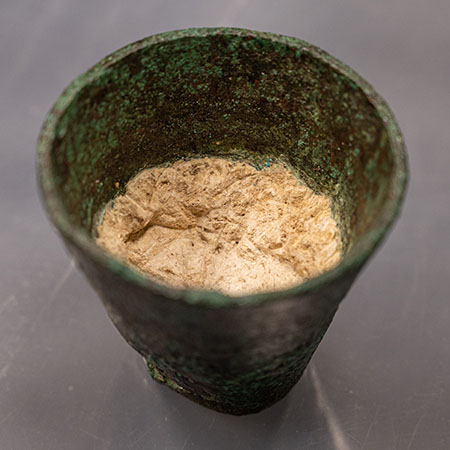An ancient brozne cup is filled with a brown waxy substance.