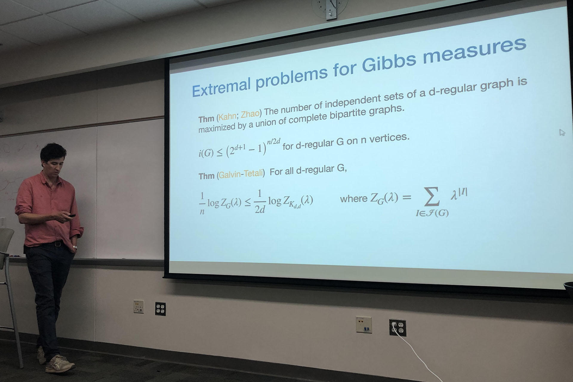 Professor standing at the front of a classroom, presenting a lecture using a projector, with slides displayed on the screen.