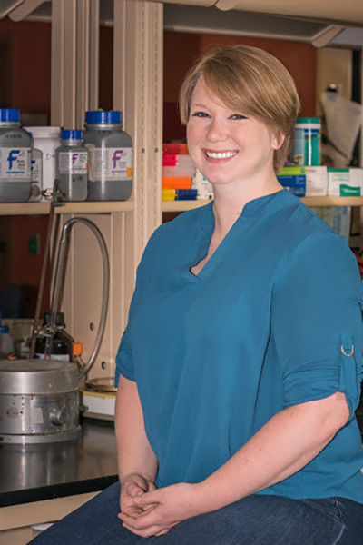 Natalie McGuire sits in a lab and smiles at the camera.