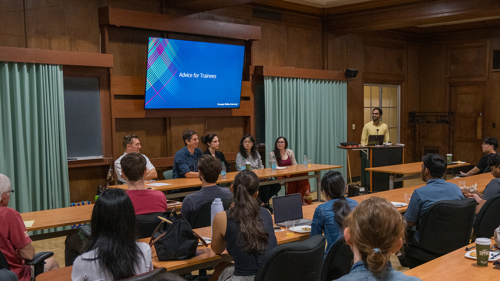 Five panelists listen to a question from a moderator as they sit in front of a room full of people.