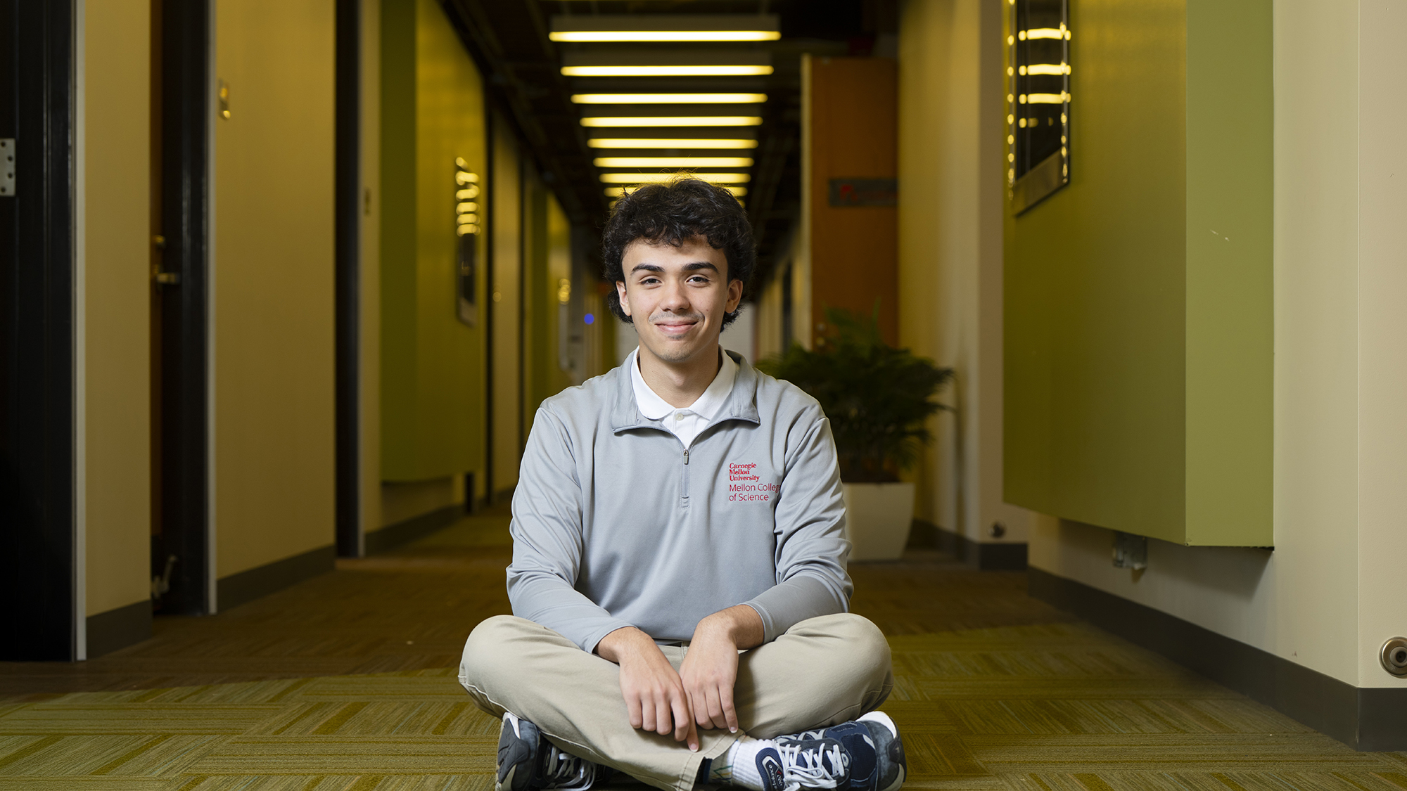 Joao Passos sits crosslegged in a hallway. He smiles at the camera.