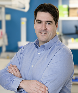Andreas Pfenning stands in his lab and smiles at the camera.