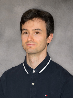 Grisha Tarnopolsky stands against a grey background and smiles at the camera.