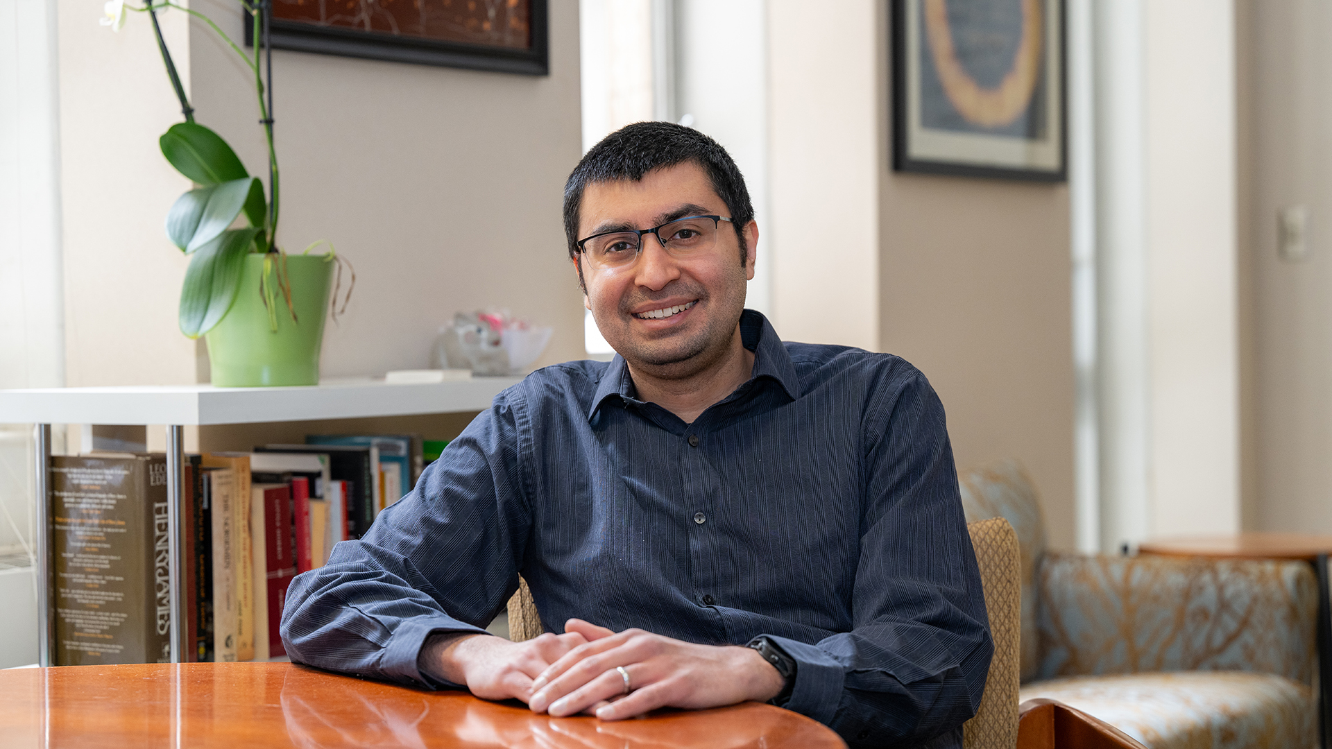 Saurabh Vyas sits at a wooden table in an office. He smiles at the camera.