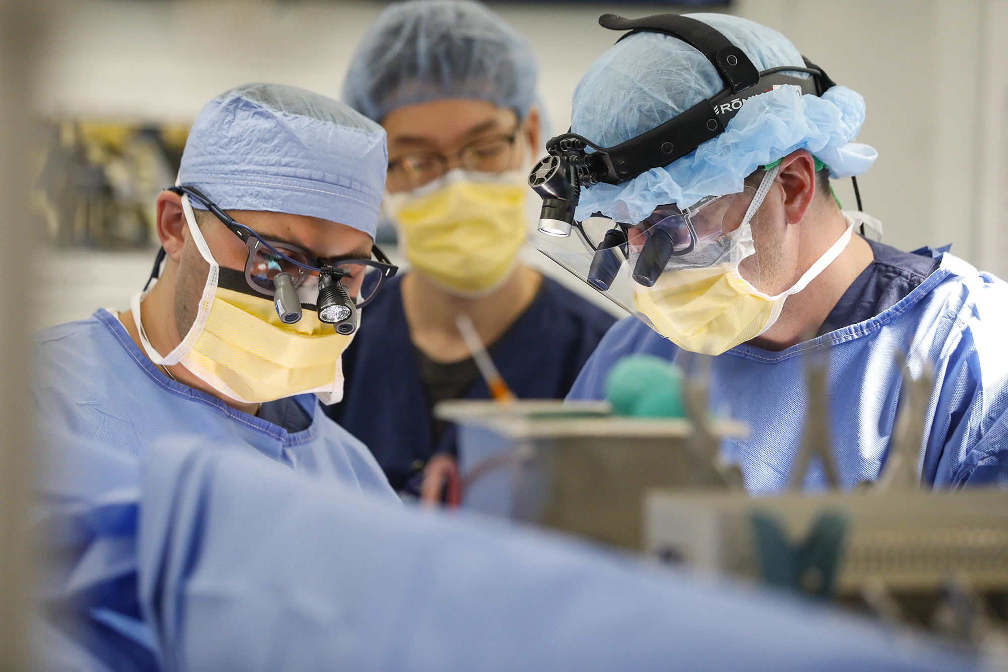 Two surgeons in scrubs and masks operate on a brain.