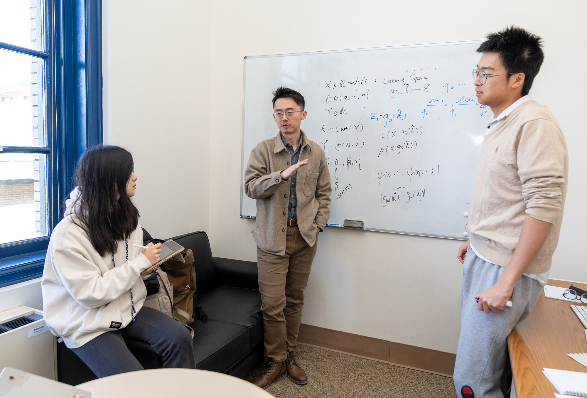 Wendy Wang, Shixiang (Woody) Zhu and Wenbin Zhou stand around a whiteboard and talk.
