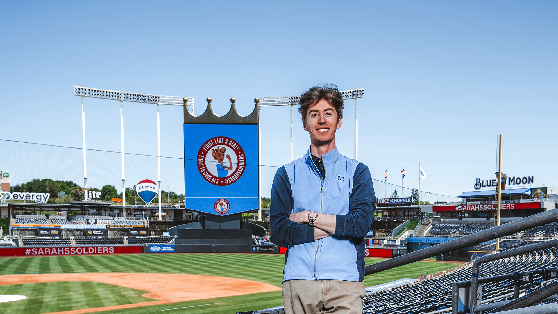 Calvin Hoffman stands in Kauffman Stadium surrounded by empty seats with the baseball diamond visible behind him.