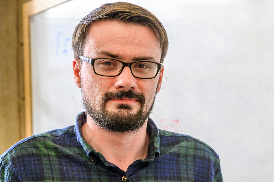 Florian Frick looks at the camera while standing in front of a white board with math equations written on it.