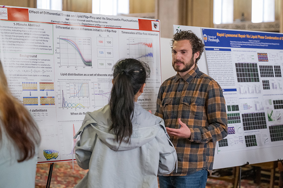 Nathaniel Wesnak stands in front of a poster presenting his research. He is talking with someone.
