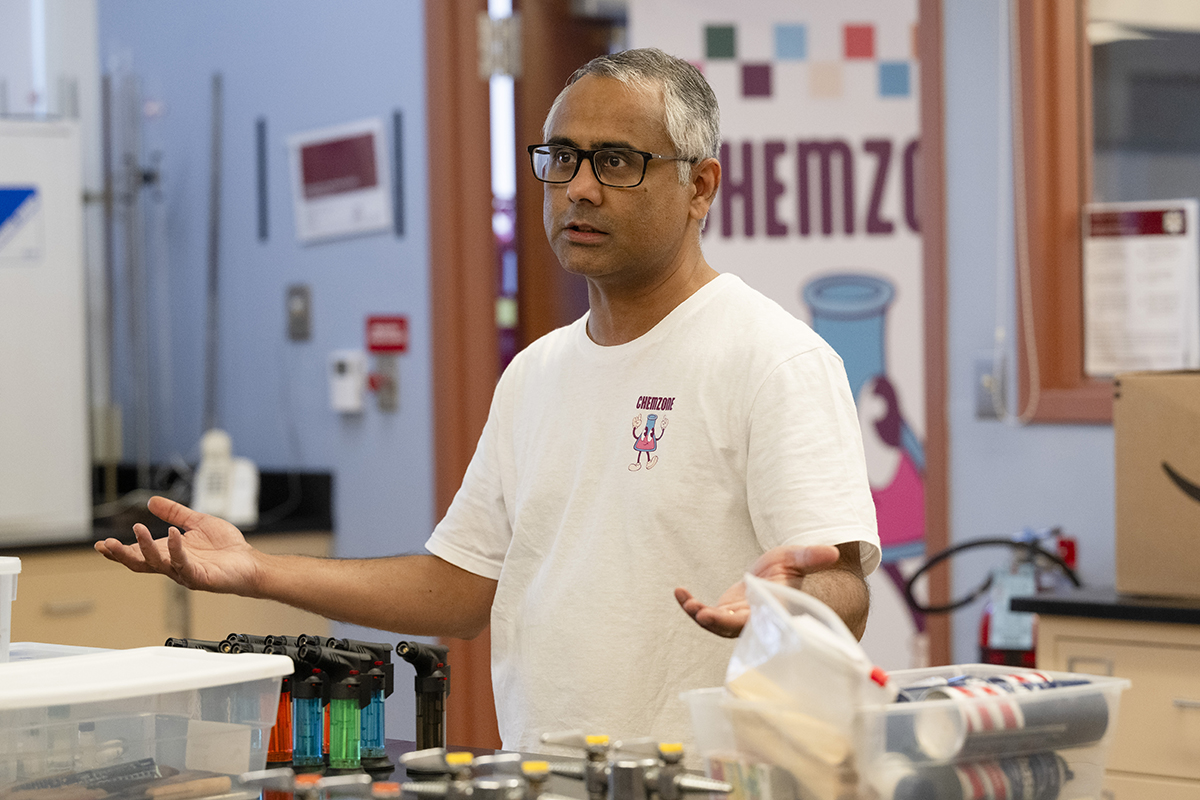 Subha Das explains an experiment during a "kitchen chemistry" session. He wears a ChemZone tee shirt and looks at some people off screen.