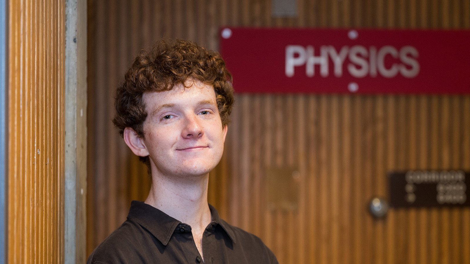 Seamus Gallagher stands next to the CMU Physics Department sign