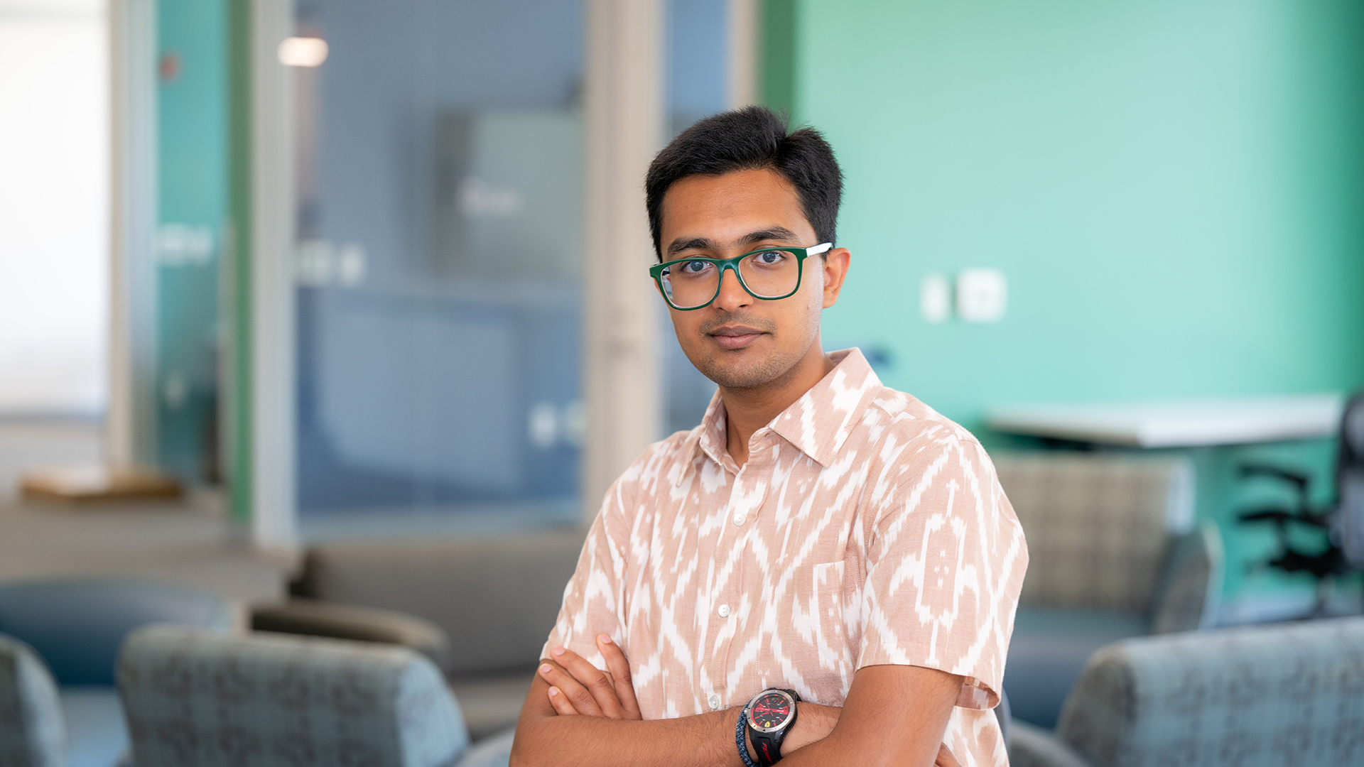 Sidharth Hariharan stands in front of a lounge with his arms crossed. He smiles at the camera.