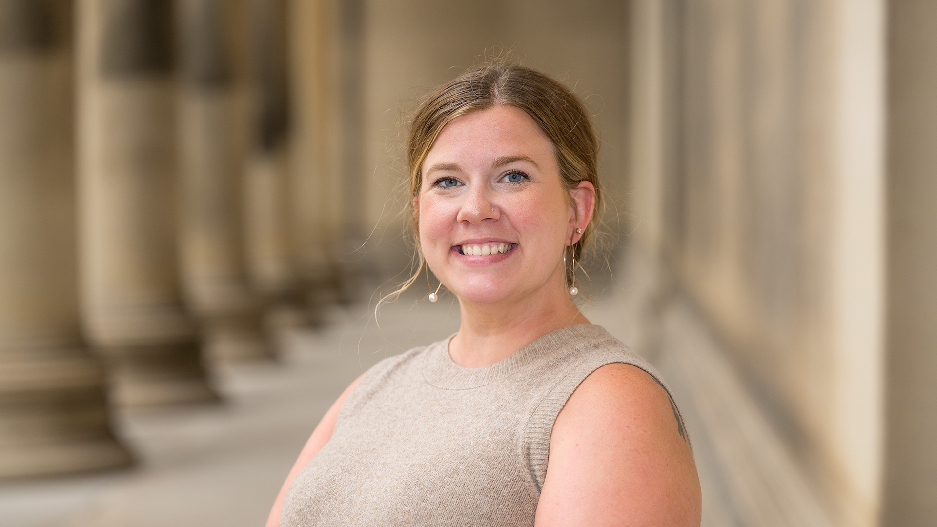 Brittany Kurtik smiles while standing in front of the Mellon Institute, wearing a beige sleeveless top, with the building's iconic columns visible in the background.